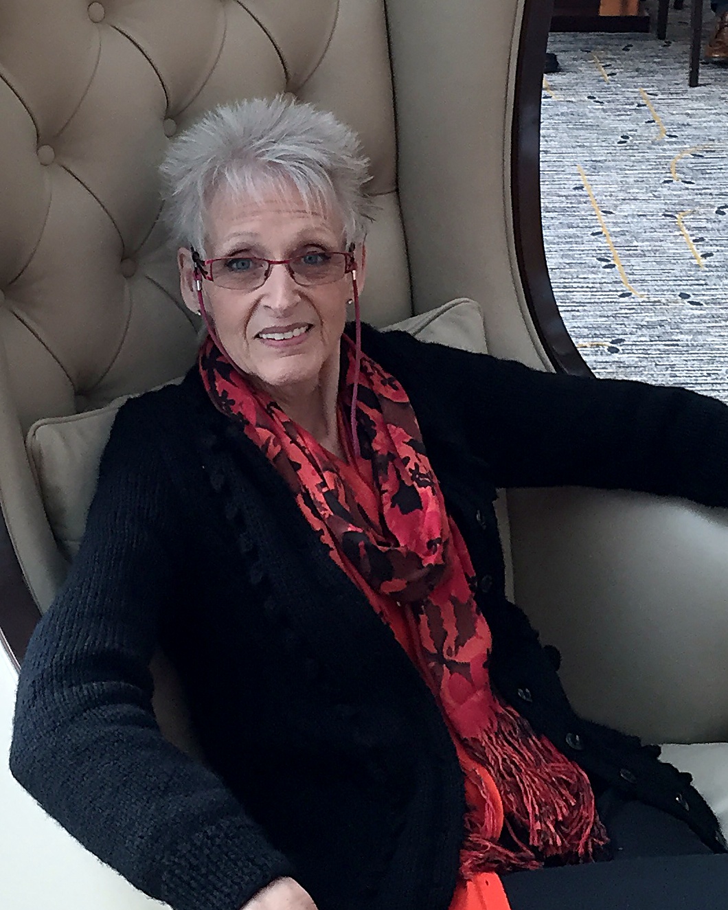 Patricia "Pat" Harford, seated, wearing a black cardigan and a red patterned scarf.